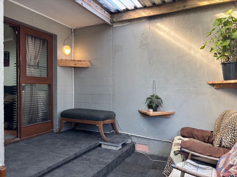 A covered patio area featuring concrete block walls, timber shelving, and a timber-framed glass door leading to the interior.