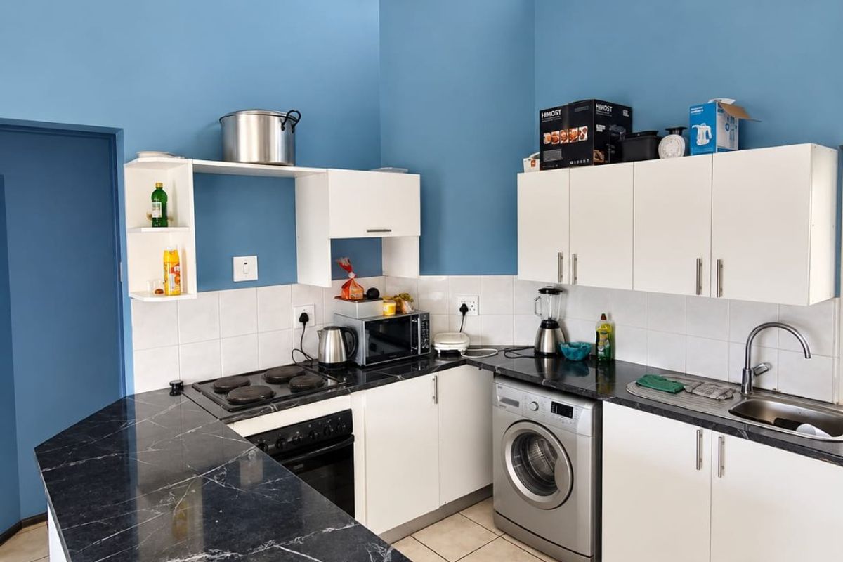 A functional kitchen featuring white cabinetry, black marble-effect countertops, an electric hob, built-in oven, and integrated laundry space with tiled flooring.
