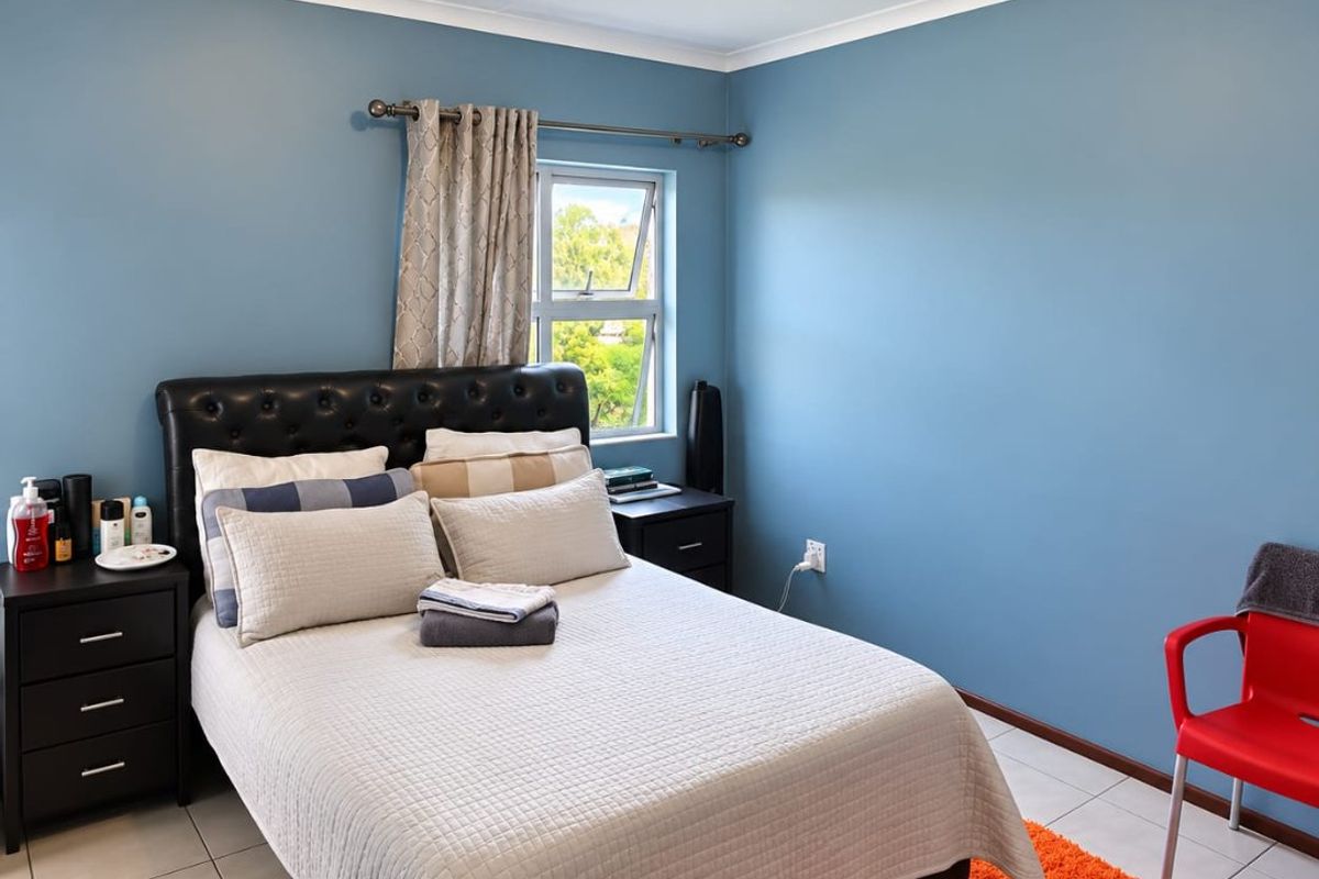 A well-lit bedroom featuring tiled flooring, a standard casement window, and a simple ceiling light fixture.