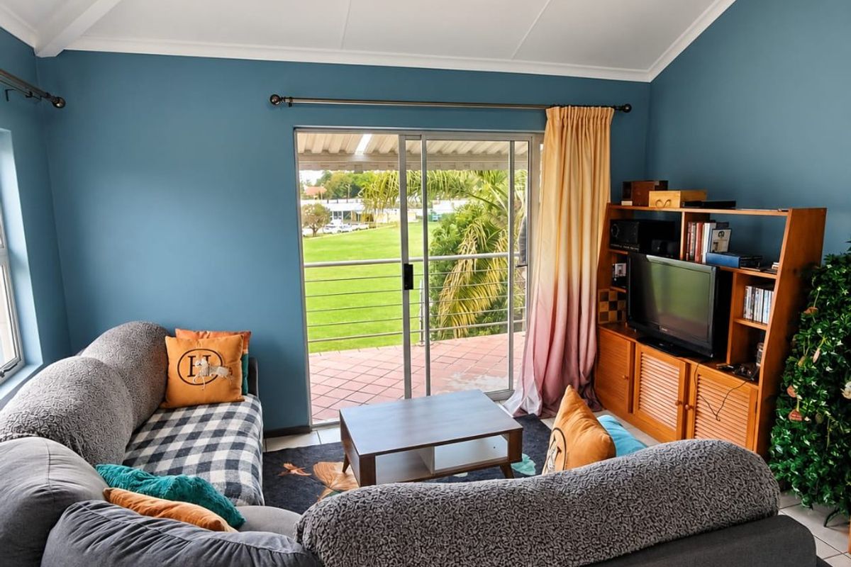A comfortable living room featuring a vaulted ceiling, tiled flooring, and a sliding glass door that opens onto a balcony with garden views.