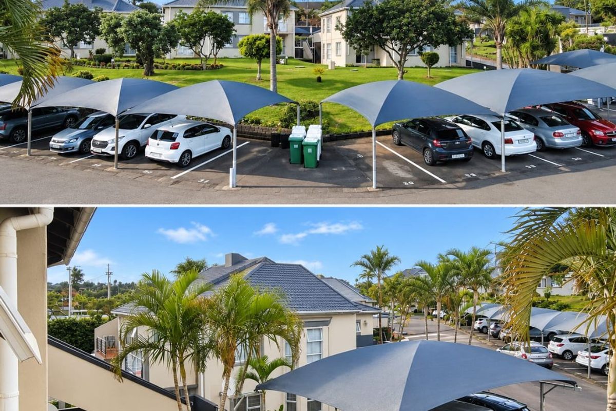 A view of the townhouse complex featuring paved parking areas with shade sails, well-maintained communal gardens, and exterior building architecture.