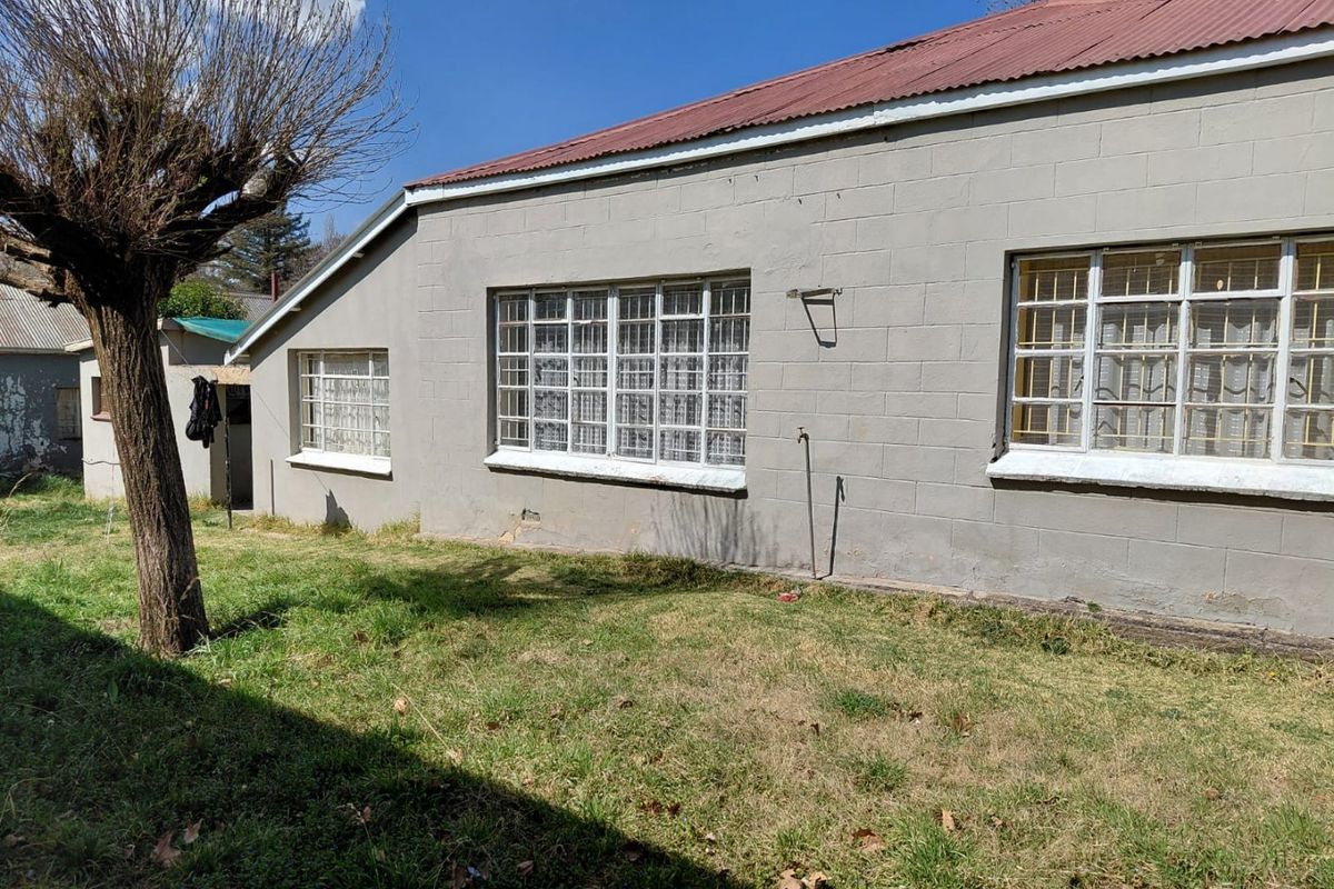 Rear exterior view of a concrete block house featuring a corrugated metal roof and steel security bars on the windows.