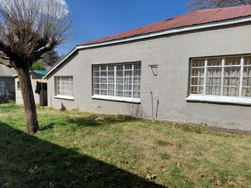 Rear exterior view of a concrete block house featuring a corrugated metal roof and steel security bars on the windows.
