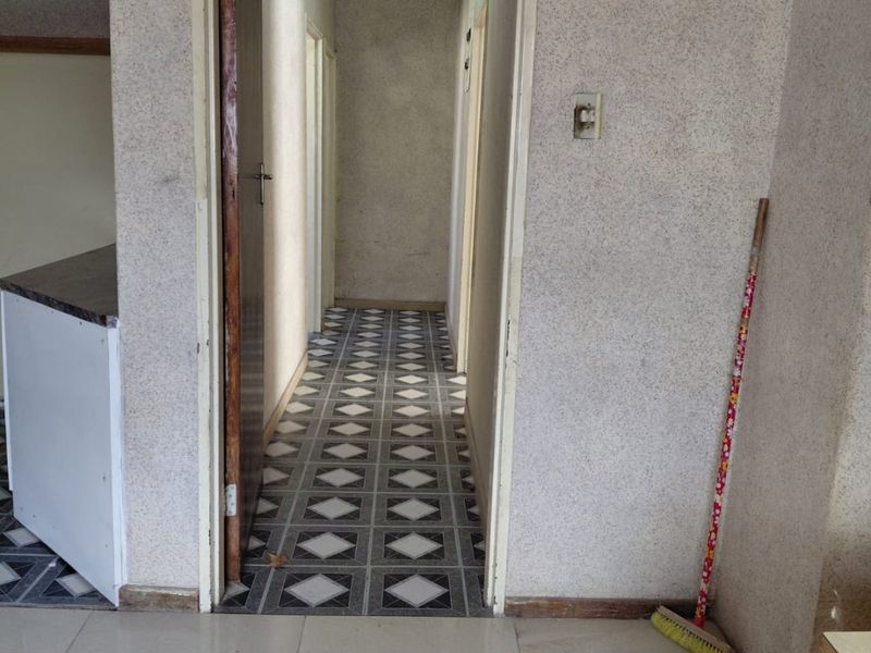 A narrow interior hallway featuring textured wall finishes and patterned floor tiles, providing access to adjacent rooms.