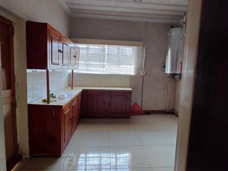 A functional kitchen space featuring built-in wooden cabinetry, tiled flooring, and a wall-mounted electric water heater, offering a blank canvas for potential renovation.