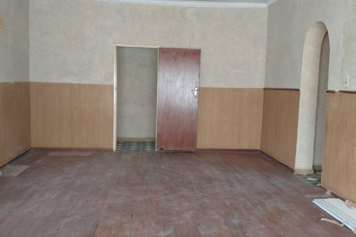 An empty living room featuring timber wall paneling, decorative ceiling molding, and an arched doorway, providing a blank canvas for renovation.