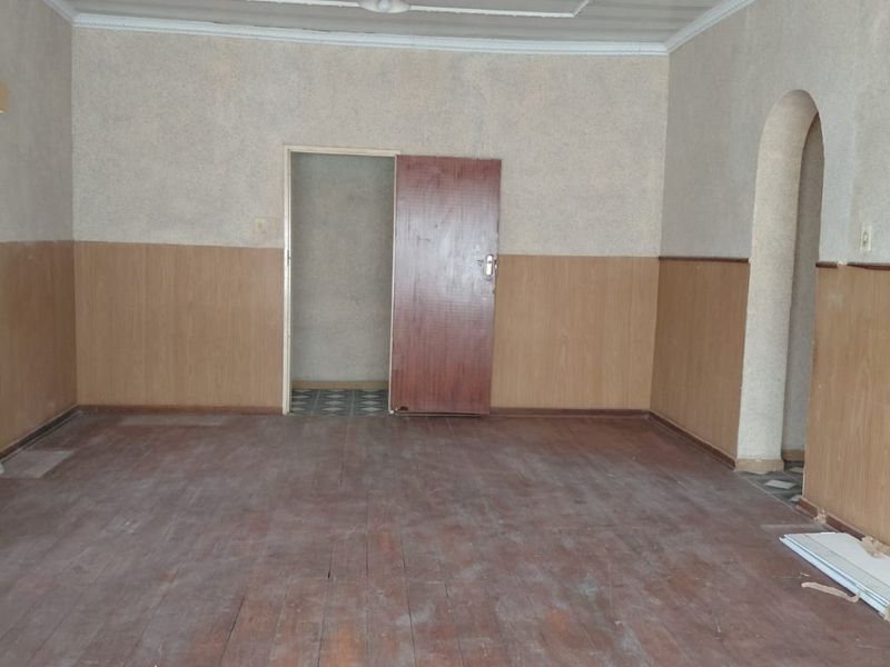 An empty living room featuring timber wall paneling, decorative ceiling molding, and an arched doorway, providing a blank canvas for renovation.