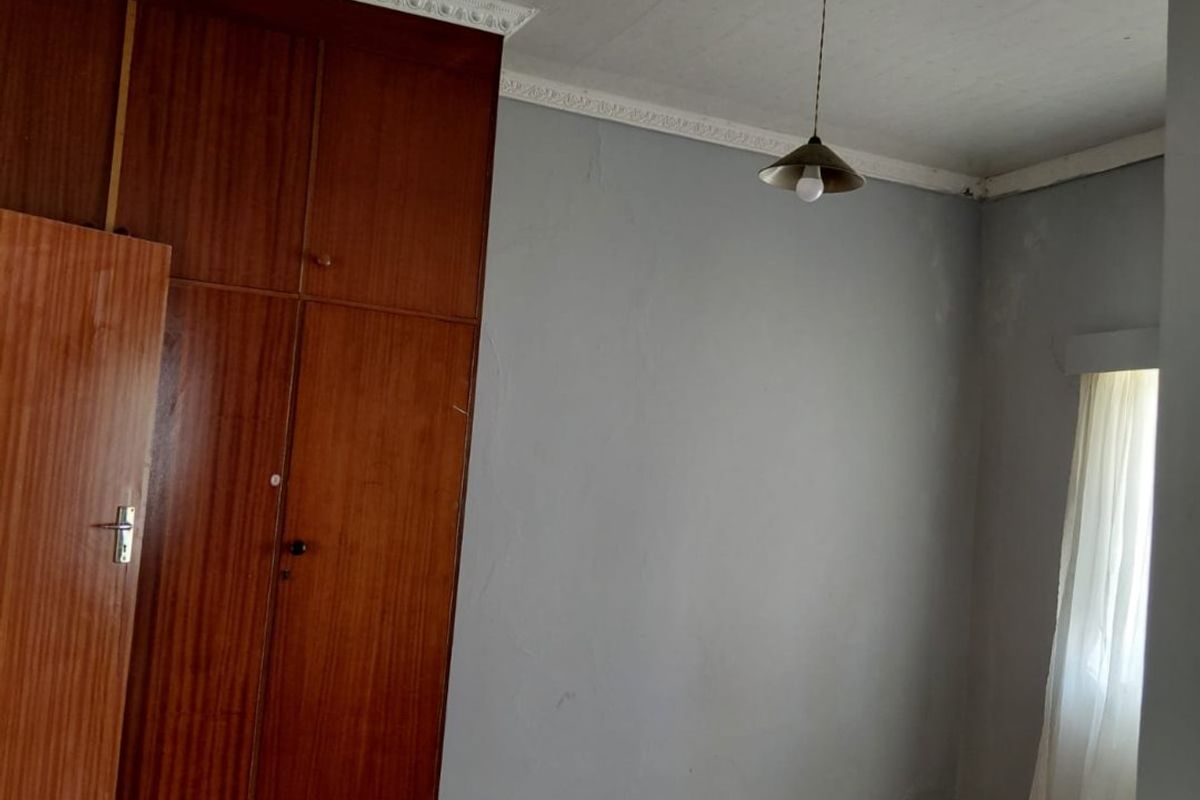 A vacant bedroom featuring original timber flooring, built-in wooden cabinetry, and decorative ceiling cornicing, offering a blank canvas for renovation.