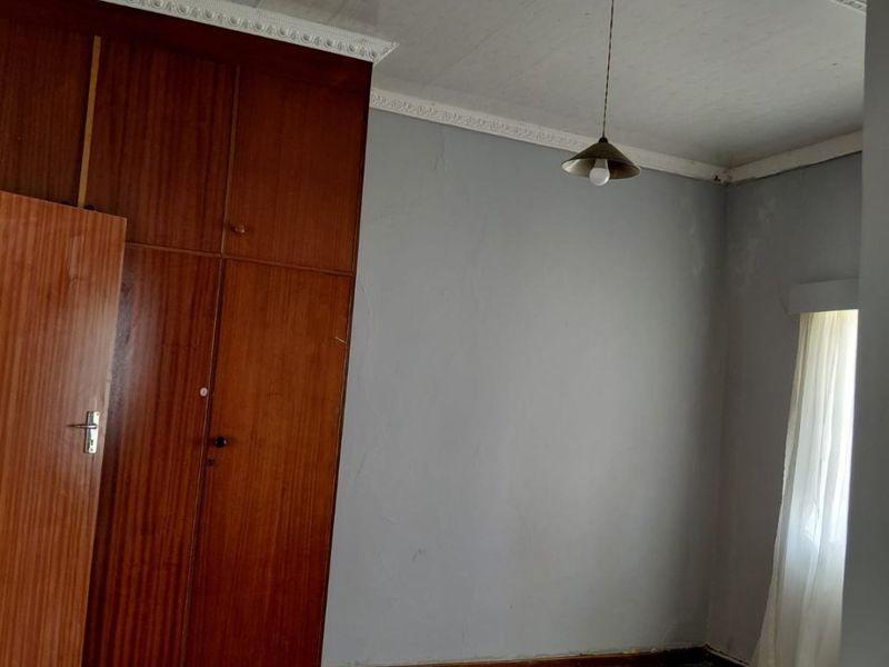 A vacant bedroom featuring original timber flooring, built-in wooden cabinetry, and decorative ceiling cornicing, offering a blank canvas for renovation.