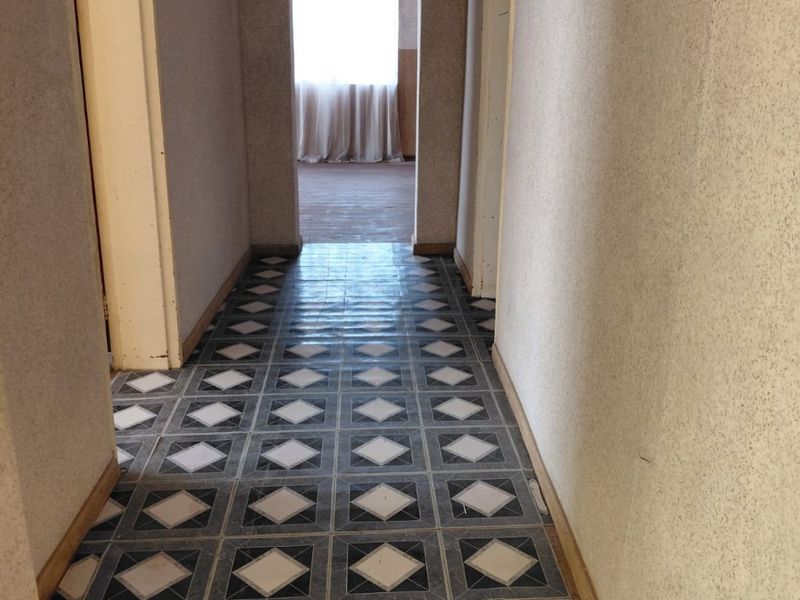 A vacant hallway featuring an arched doorway and classic patterned floor tiles, leading into an adjacent room.