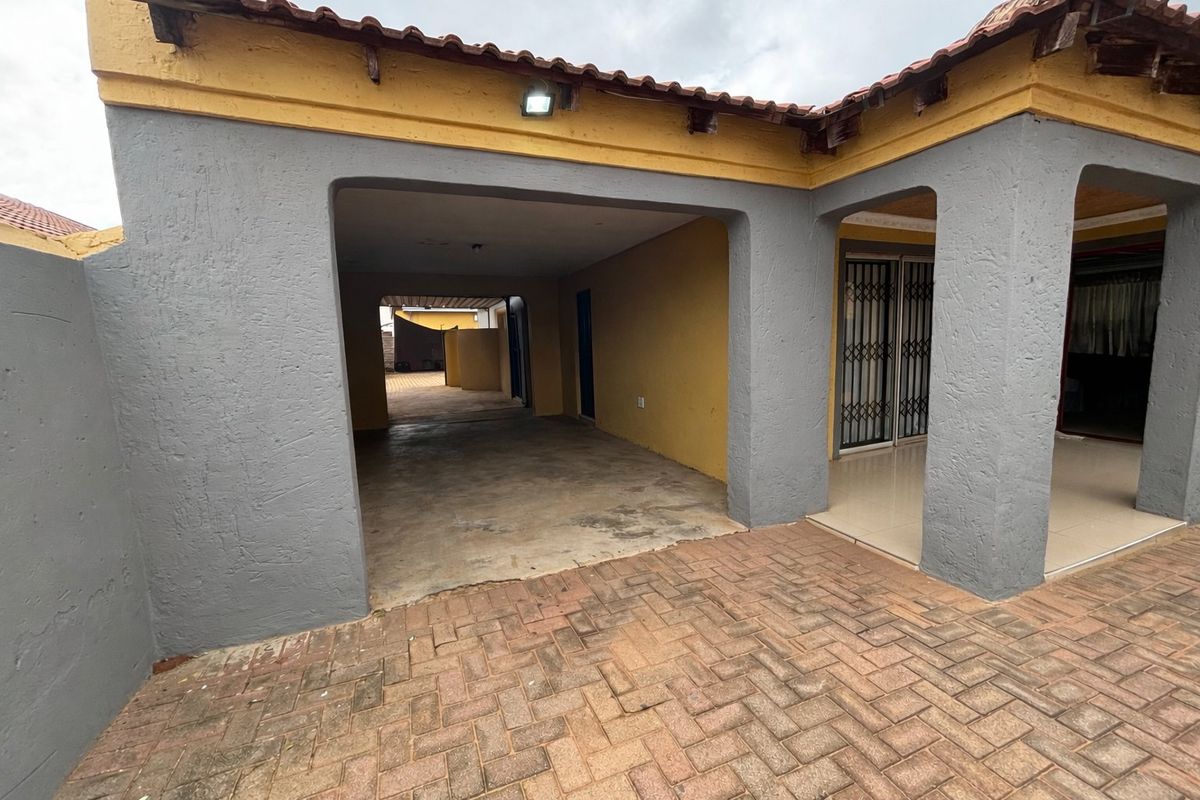 A covered patio area with paved flooring and a security gate entrance, featuring a neutral grey and yellow exterior finish.