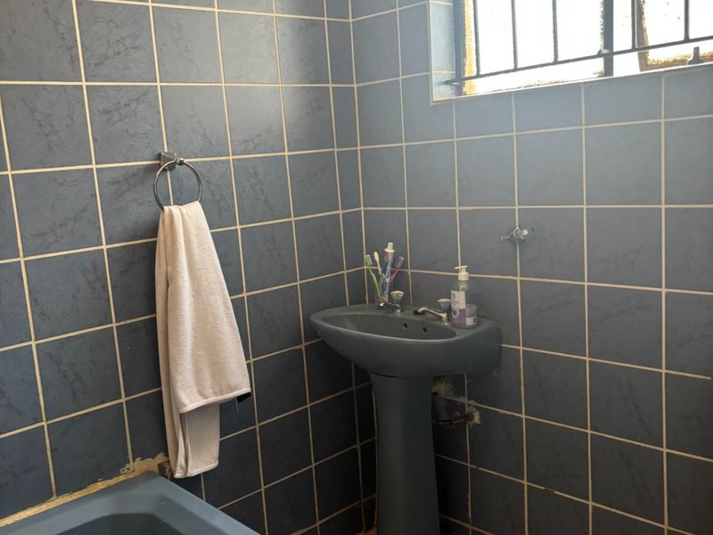 A dated bathroom featuring blue sanitaryware, full-height blue wall tiling, and tiled flooring, requiring modernization and maintenance of finishes.