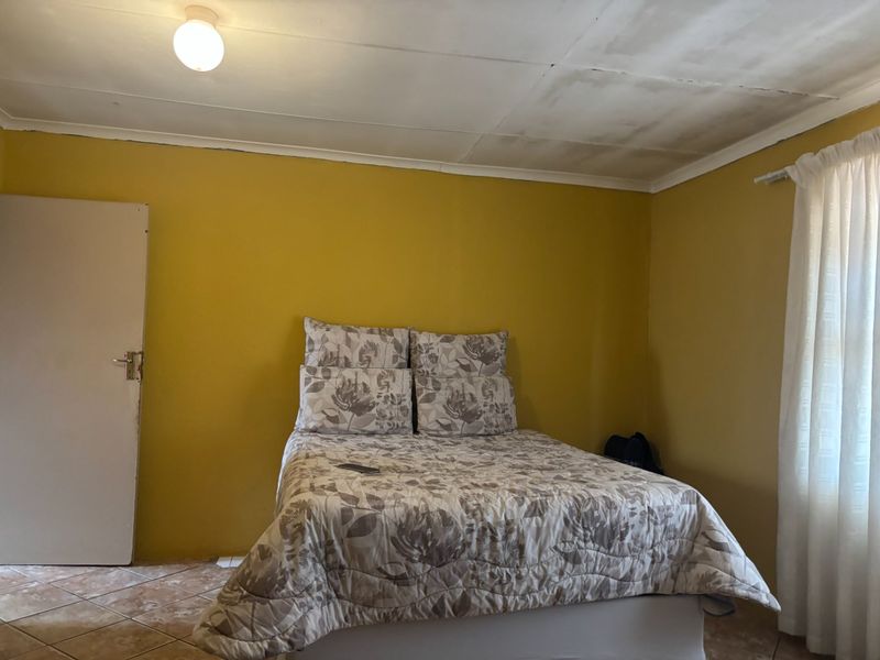 A bedroom featuring tiled flooring and yellow painted walls, requiring some ceiling maintenance and cosmetic updates to improve the overall aesthetic.