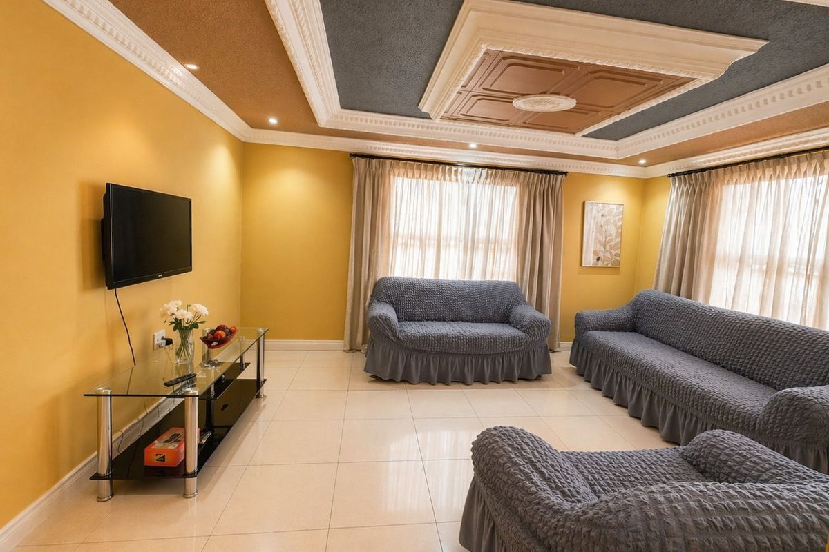 A spacious living room featuring tiled flooring, decorative ceiling molding with recessed lighting, and large windows with curtain tracks.