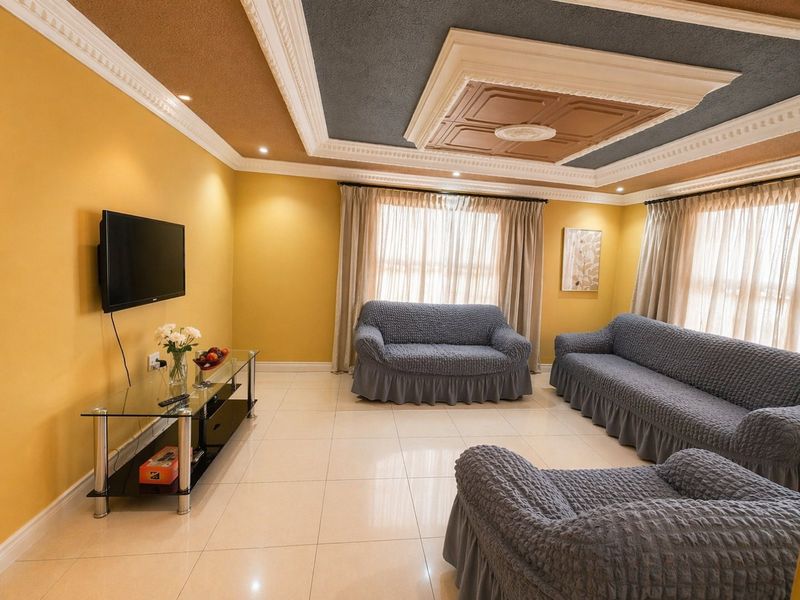 A spacious living room featuring tiled flooring, decorative ceiling molding with recessed lighting, and large windows with curtain tracks.