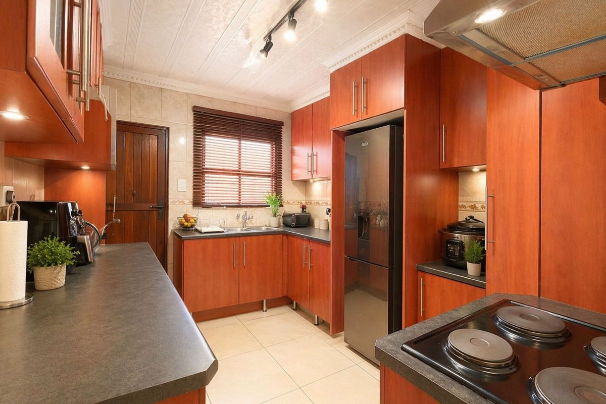 A well-maintained kitchen featuring warm-toned laminate cabinetry, dark countertops, tiled backsplash, and integrated electric hob with overhead extractor fan.