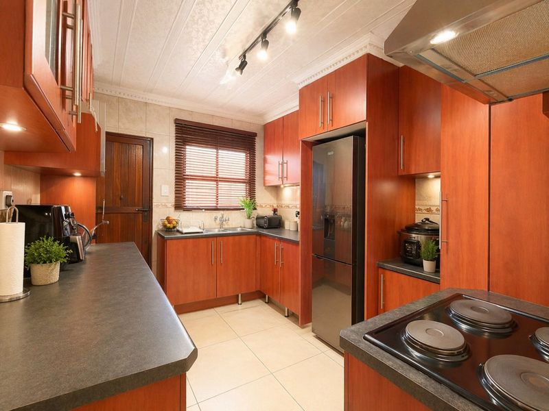 A well-maintained kitchen featuring warm-toned laminate cabinetry, dark countertops, tiled backsplash, and integrated electric hob with overhead extractor fan.