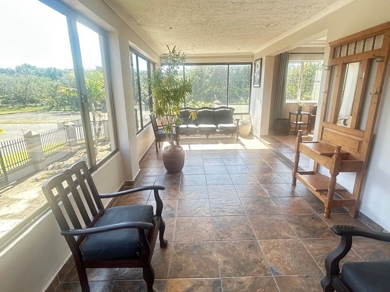 A spacious, enclosed sunroom or patio area featuring large windows, tiled flooring, and a textured ceiling, offering ample natural light and garden views.