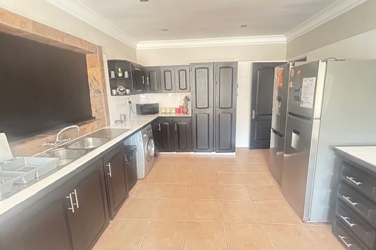 A functional kitchen featuring dark cabinetry, tiled flooring, and a double sink with a stone-look splashback, offering ample storage and workspace.
