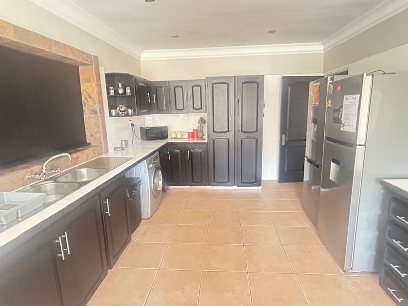 A functional kitchen featuring dark cabinetry, tiled flooring, and a double sink with a stone-look splashback, offering ample storage and workspace.