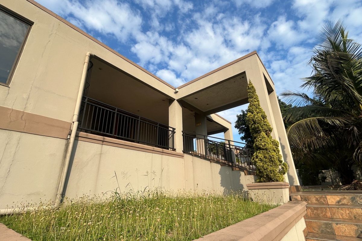 A low-angle view of the rear exterior featuring a covered patio with metal railings, tiled stairs, and a concrete facade under a blue sky.