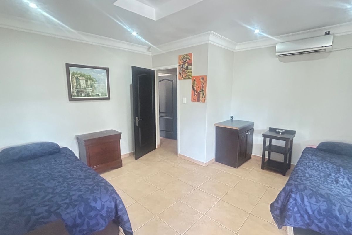 A spacious bedroom featuring tiled flooring, recessed ceiling lighting, cove molding, and a wall-mounted split-system air conditioning unit.