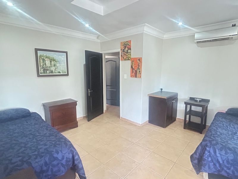 A spacious bedroom featuring tiled flooring, recessed ceiling lighting, cove molding, and a wall-mounted split-system air conditioning unit.