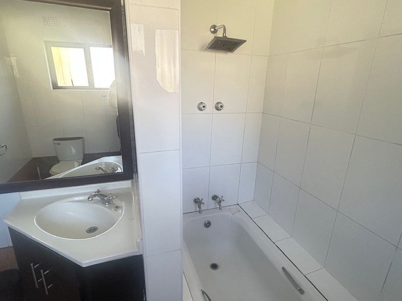 A functional bathroom featuring a vanity with basin, a bathtub with shower head, and a toilet, finished with white wall tiles.