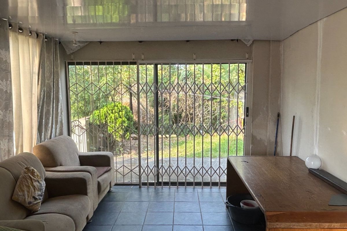 Living area featuring tiled flooring, a glossy ceiling, and a sliding glass door with a security gate leading to the garden.