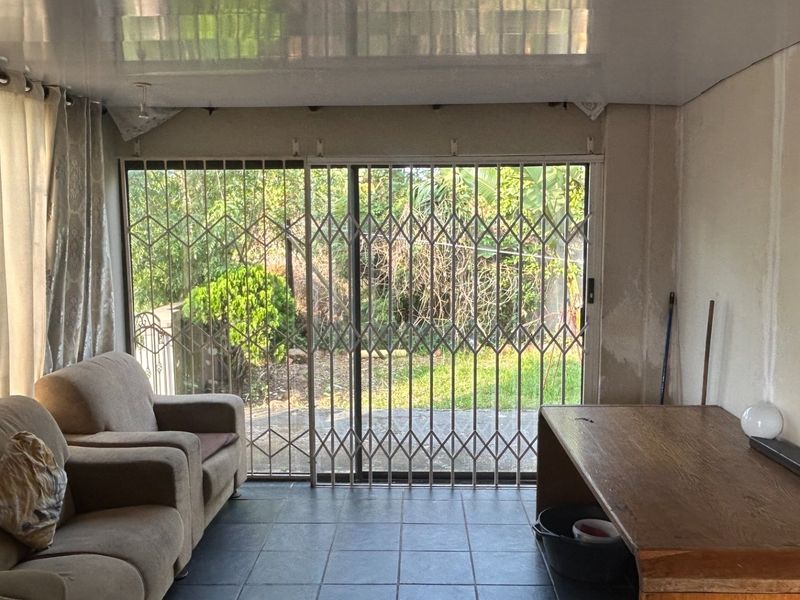 Living area featuring tiled flooring, a glossy ceiling, and a sliding glass door with a security gate leading to the garden.