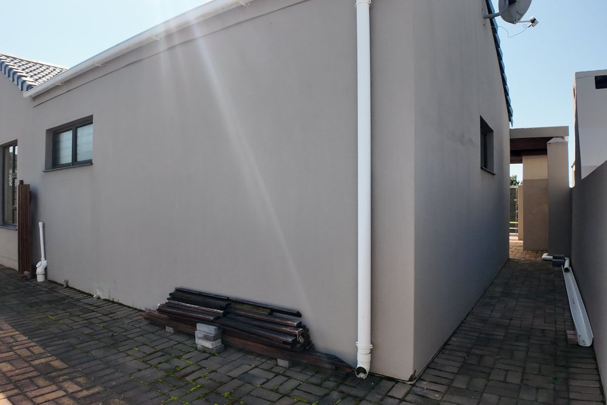 A view of the rear exterior wall and paved side walkway of the property, featuring a clean plastered finish and functional drainage downpipes.