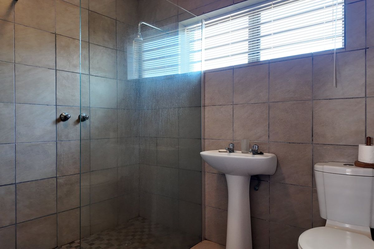 A functional bathroom featuring a pedestal basin, a glass-enclosed shower, and neutral wall tiling with a window for natural light.