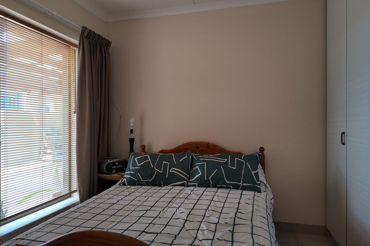 A functional bedroom featuring built-in wardrobes, tiled flooring, and a window fitted with venetian blinds and curtain tracks.