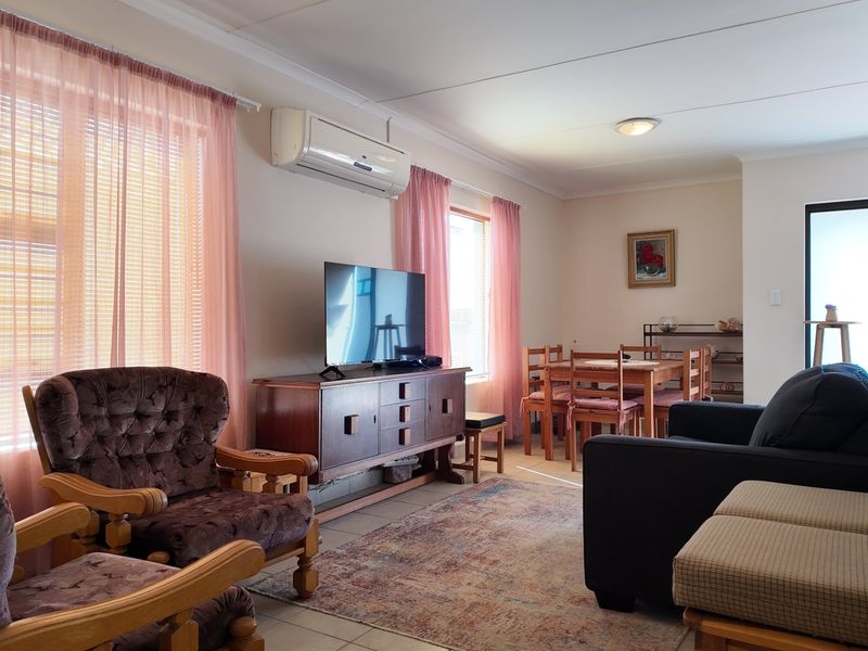 Open-plan living and dining area featuring tiled flooring, a wall-mounted air conditioning unit, and neutral wall finishes.