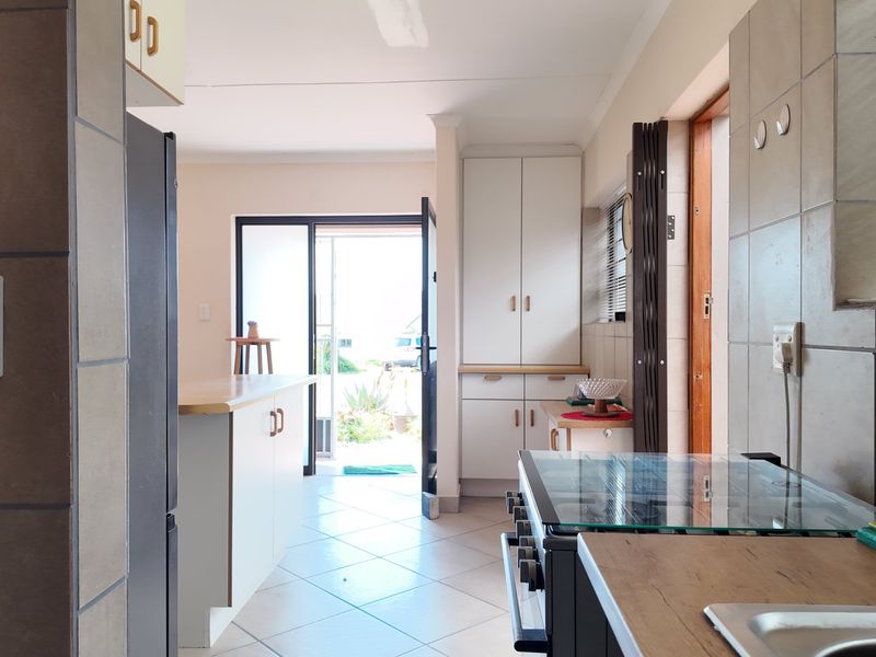 A functional kitchen featuring built-in cabinetry, laminate countertops, a freestanding stove, and tiled flooring, with direct access to the outdoor area.