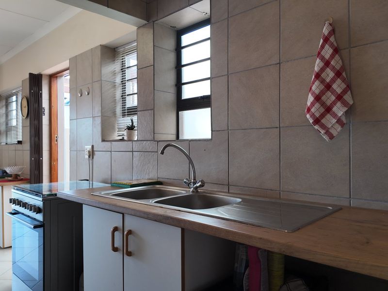 A functional kitchen featuring a stainless steel double sink, tiled splashback, timber-look countertops, and built-in cabinetry with a freestanding stove.