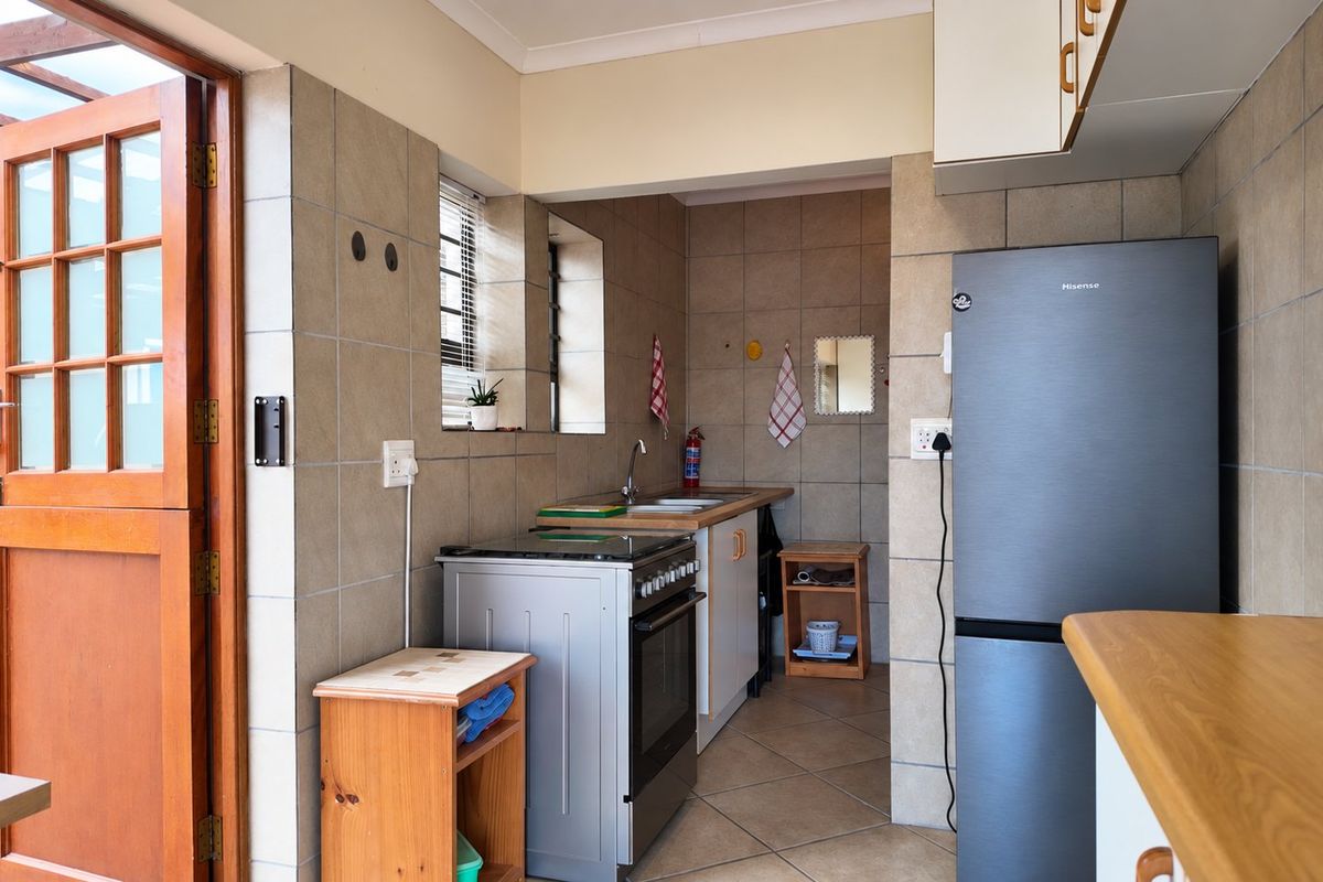 A functional kitchen featuring tiled walls and flooring, built-in cabinetry, a stainless steel sink, and a freestanding stove with direct access to an outdoor area.