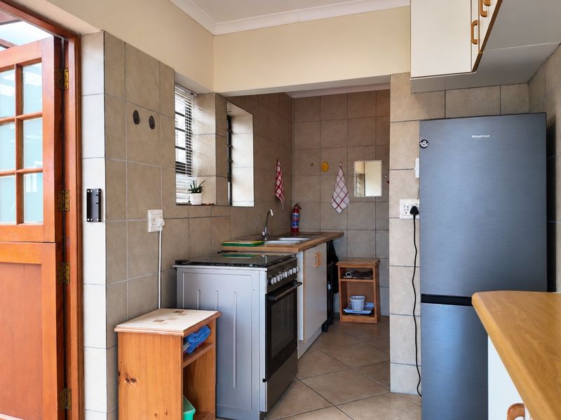 A functional kitchen featuring tiled walls and flooring, built-in cabinetry, a stainless steel sink, and a freestanding stove with direct access to an outdoor area.