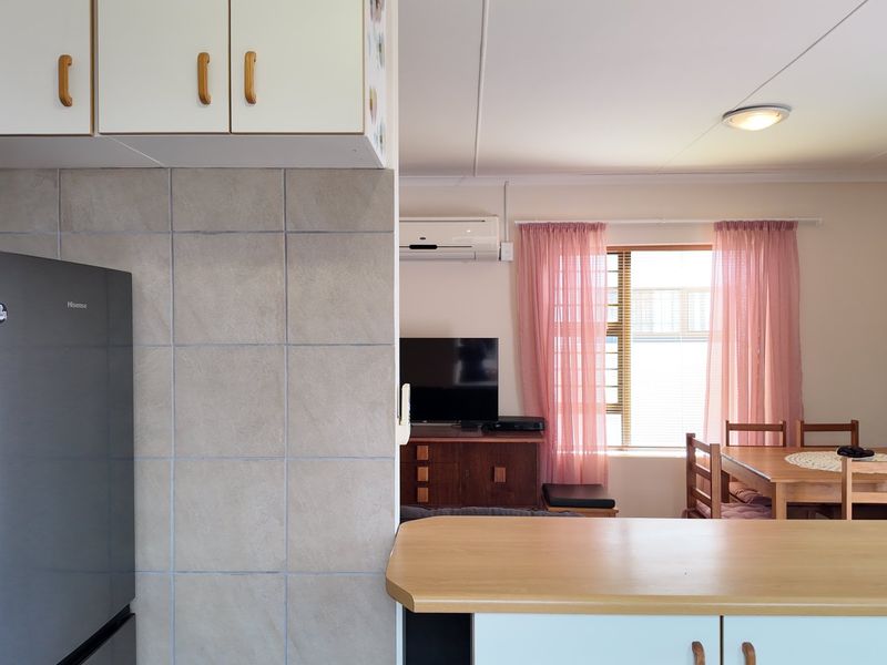 Open-plan living area featuring a functional kitchen with tiled splashback, breakfast bar, and a split-system air conditioner, flowing into the dining and lounge space.
