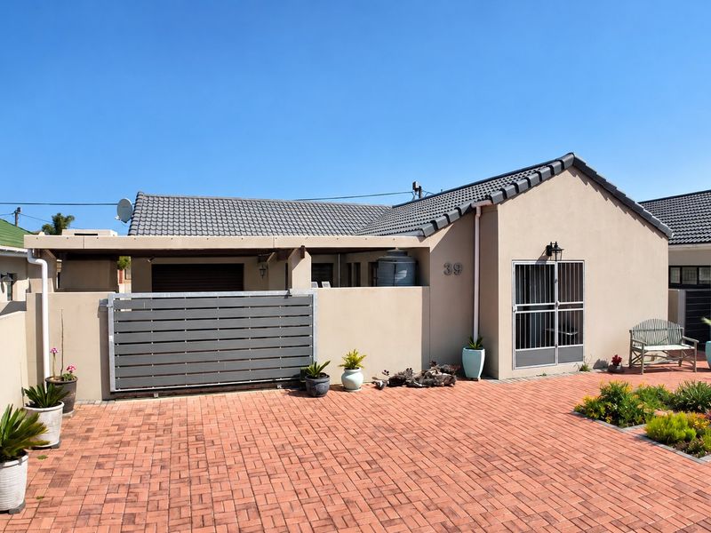 Front elevation of a single-story house featuring a paved driveway, tiled roof, and secure gated entrance.