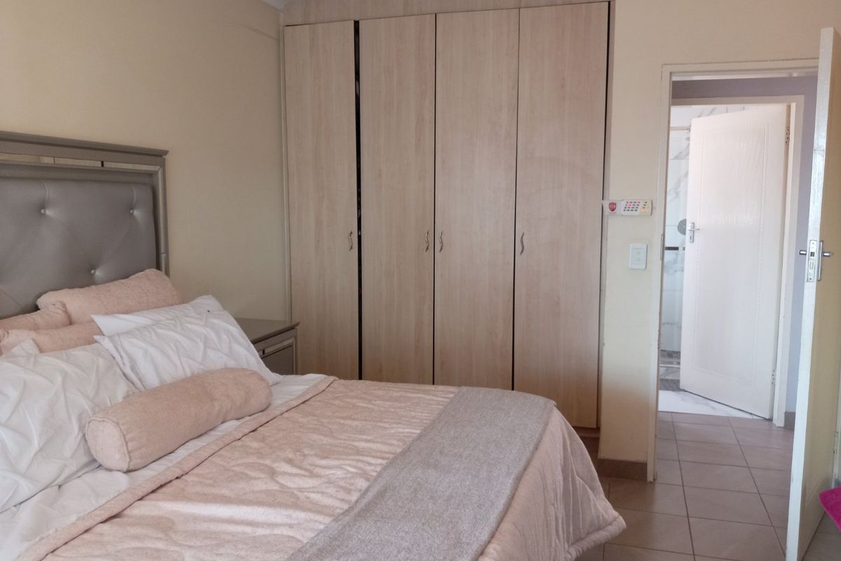 A well-maintained bedroom featuring light wood-finish built-in cupboards, tiled flooring, and direct access to an en-suite bathroom.