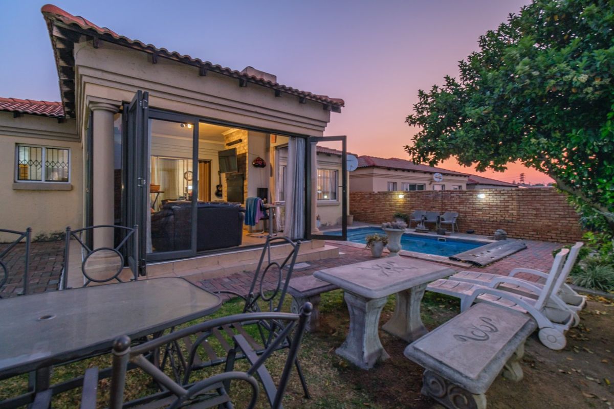 Rear exterior view featuring a swimming pool, paved patio area, and bi-fold doors leading into the living space at sunset.