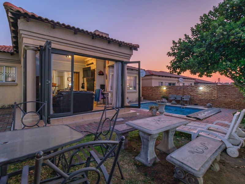 Rear exterior view featuring a swimming pool, paved patio area, and bi-fold doors leading into the living space at sunset.