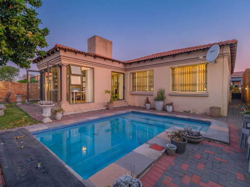 Rear exterior view featuring a swimming pool, paved patio area, and direct access to the home with security bars on windows.
