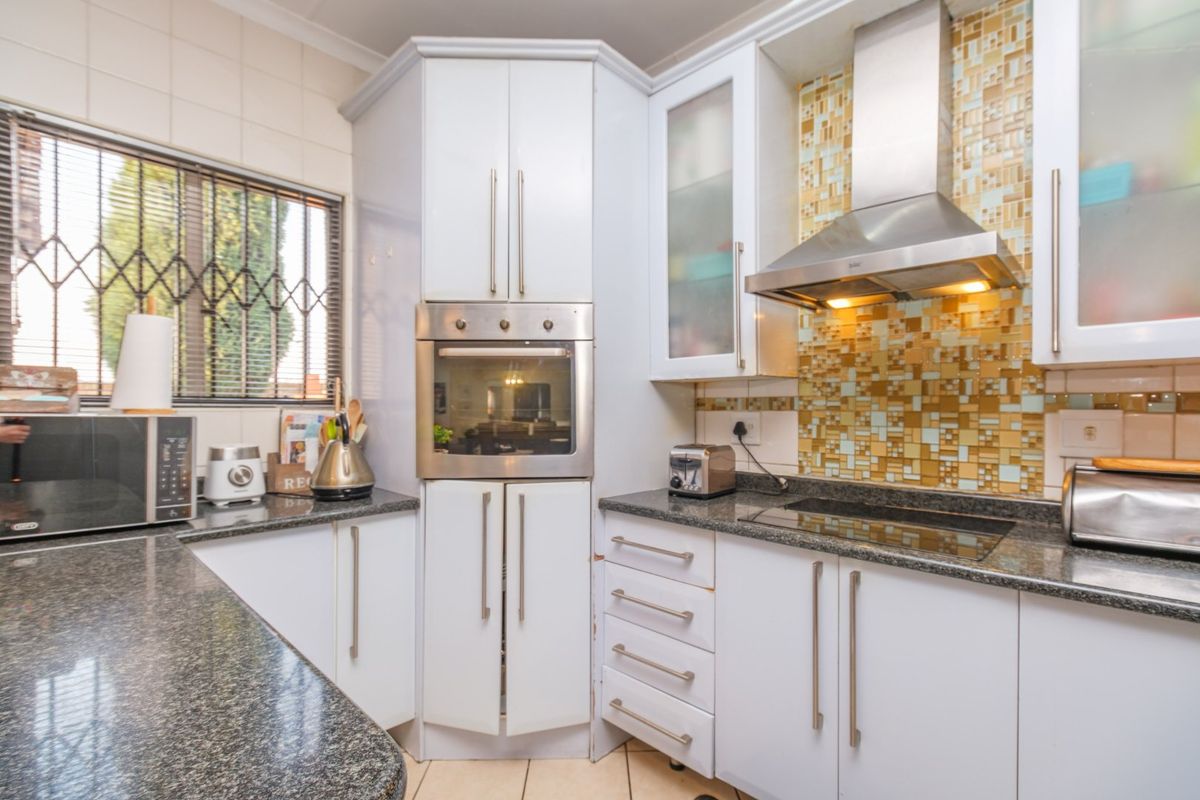 A functional kitchen featuring granite countertops, built-in oven, electric hob, stainless steel extractor fan, and a decorative mosaic tile backsplash.