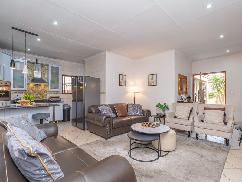 An open-plan living area featuring a modern kitchen with built-in appliances, tiled flooring, and direct access to the outdoor space.