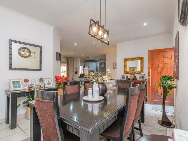 An open-plan dining area featuring tiled floors, modern pendant lighting, and a solid wood entrance door, flowing into the kitchen space.