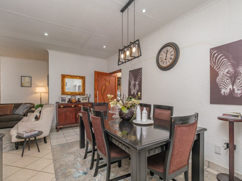 An open-plan dining and living area featuring tiled flooring, recessed downlighting, and a modern pendant light fixture over the dining space.