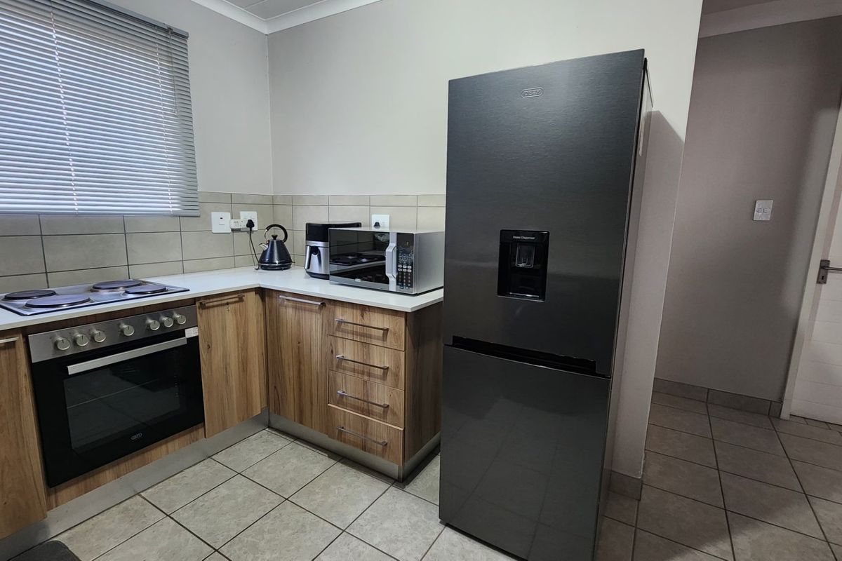 Modern kitchen featuring wood-finish cabinetry, built-in oven and hob, tiled backsplash, and neutral floor tiles.
