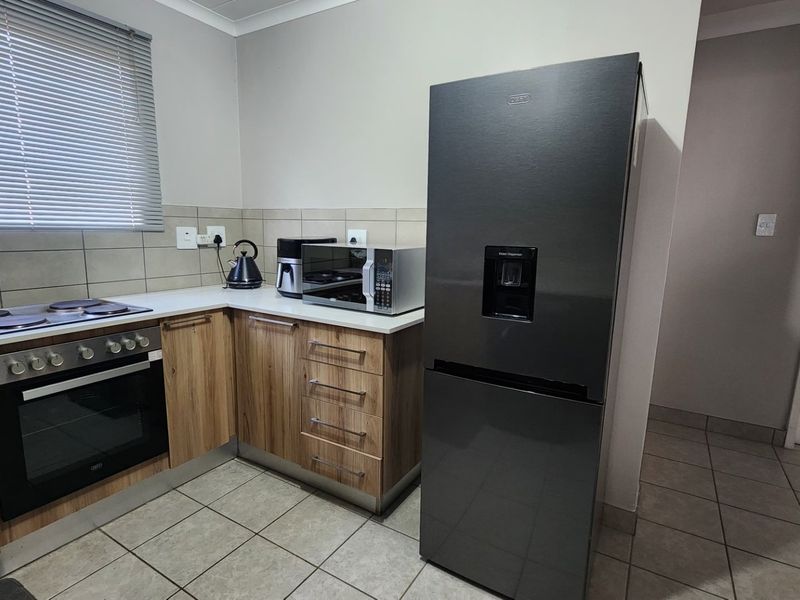 Modern kitchen featuring wood-finish cabinetry, built-in oven and hob, tiled backsplash, and neutral floor tiles.